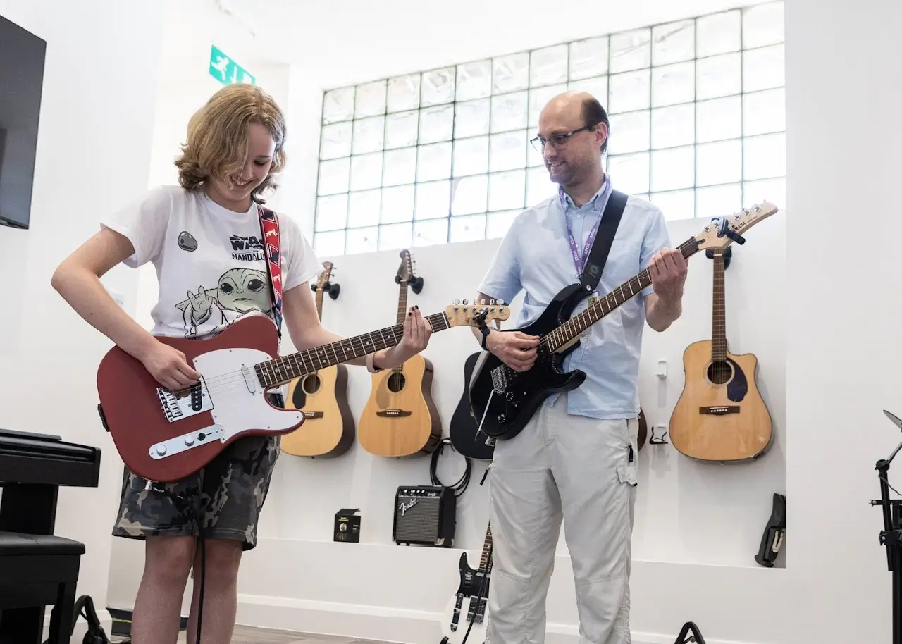 A young person learning to play the guitar with a tutor